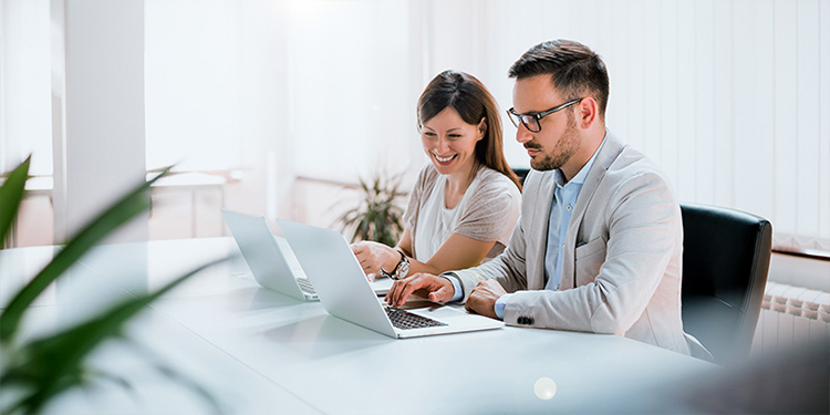 A stock photo of a businessman and a businesswoman working on their laptops.